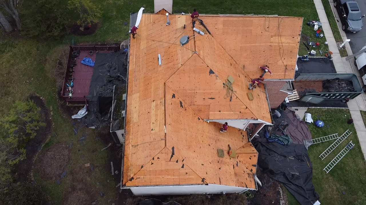 Aerial view of a roof stripped to the bare plywood deck with the crew working on it