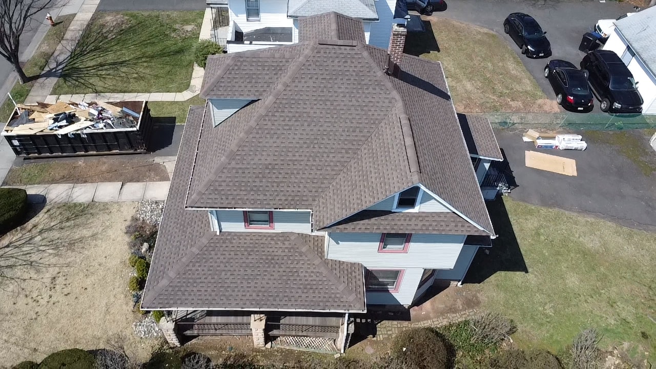 Finished brown shingle roof with a dumpster of old roofing at the curb
